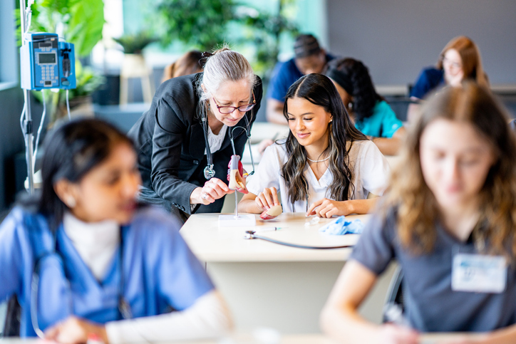 A nurse educator helps a student in a classroom